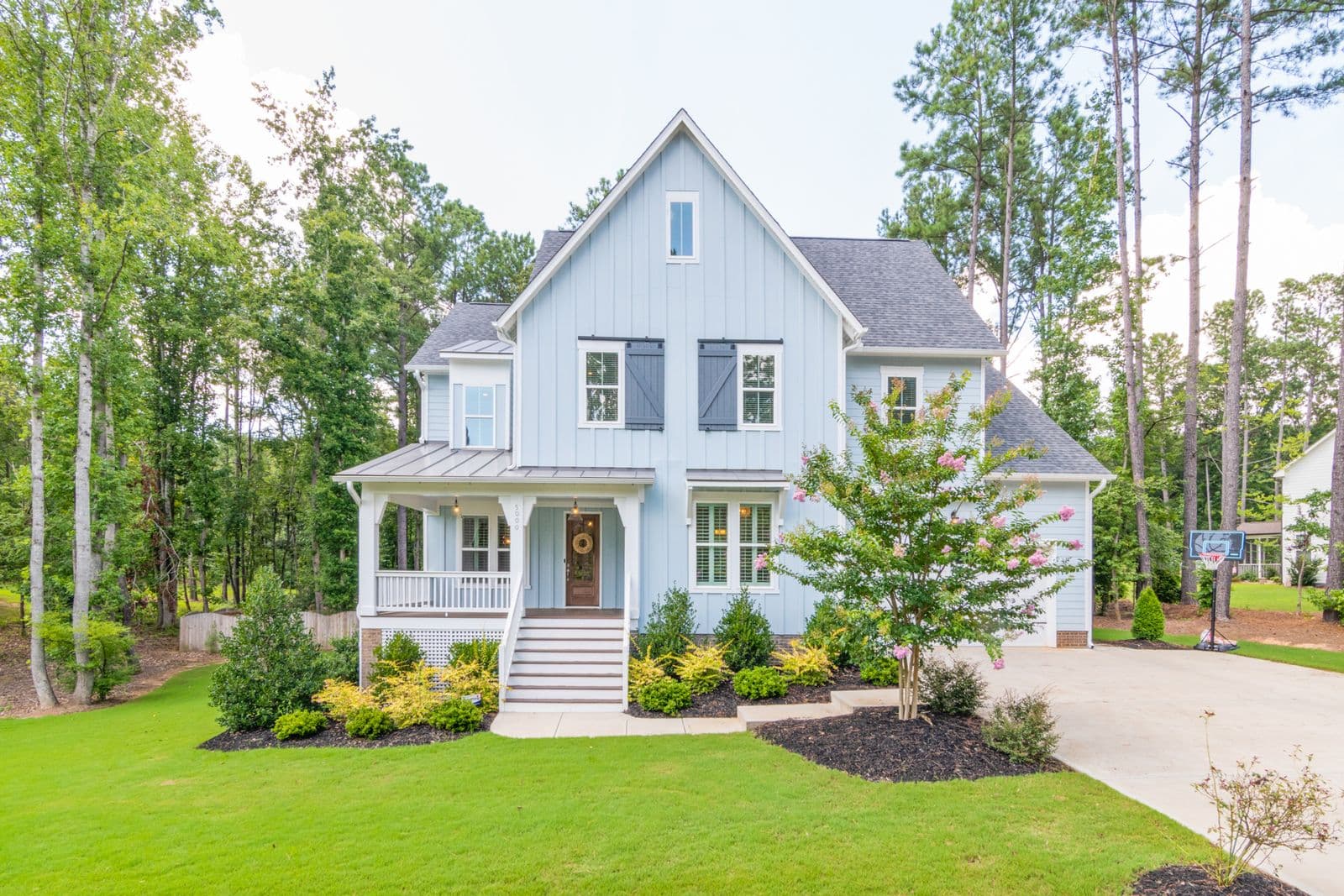 A white modern farmhouse with a front porch, set among tall pines under a blue sky